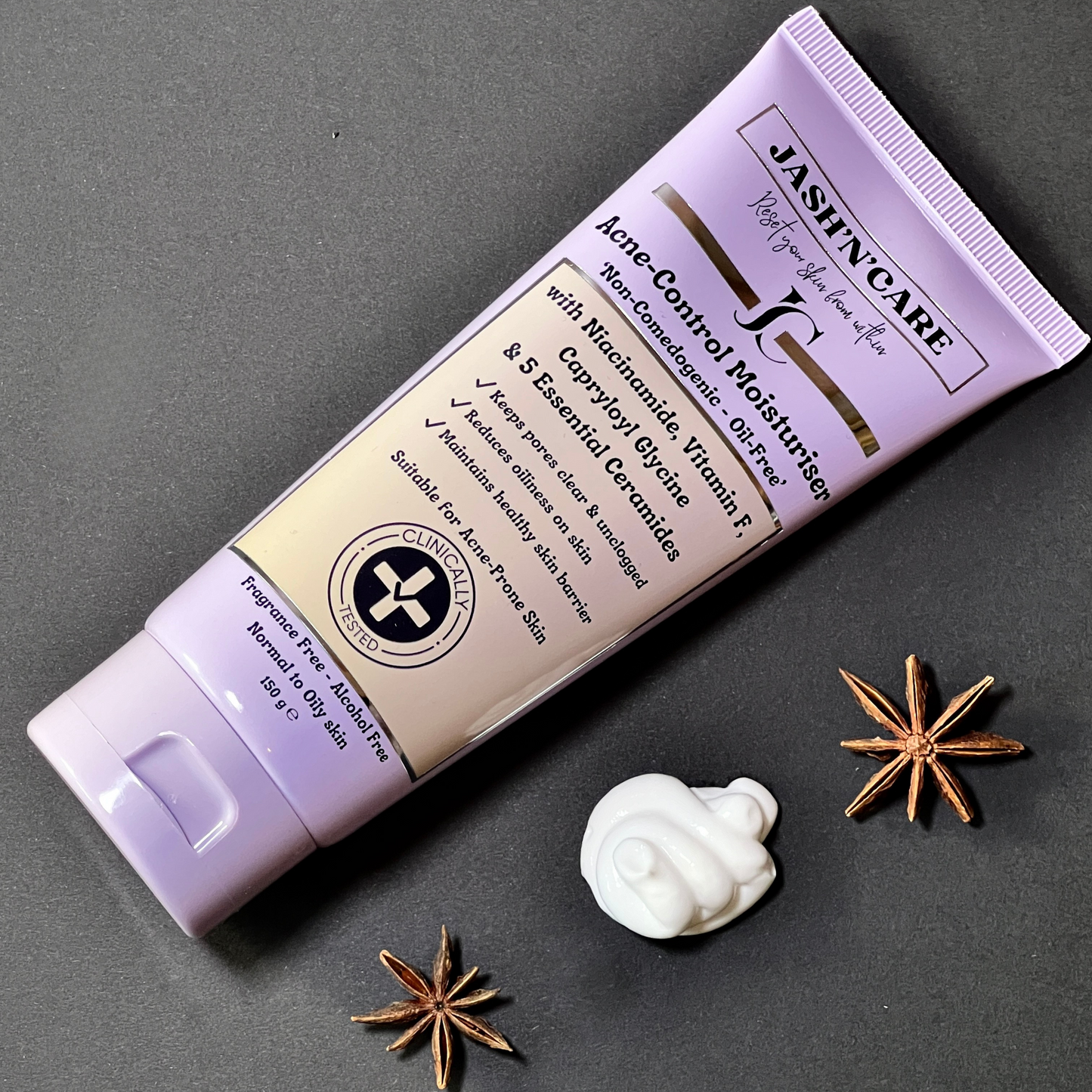 Jashn’Care Acne-Control Moisturizer tube lying diagonally on a gray background, surrounded by star anise and a swirl of cream. Product highlights include niacinamide, vitamin F, capryloyl glycine, and 5 essential ceramides. Text on packaging promotes its non-comedogenic, oil-free, alcohol-free formulation suitable for acne-prone skin.